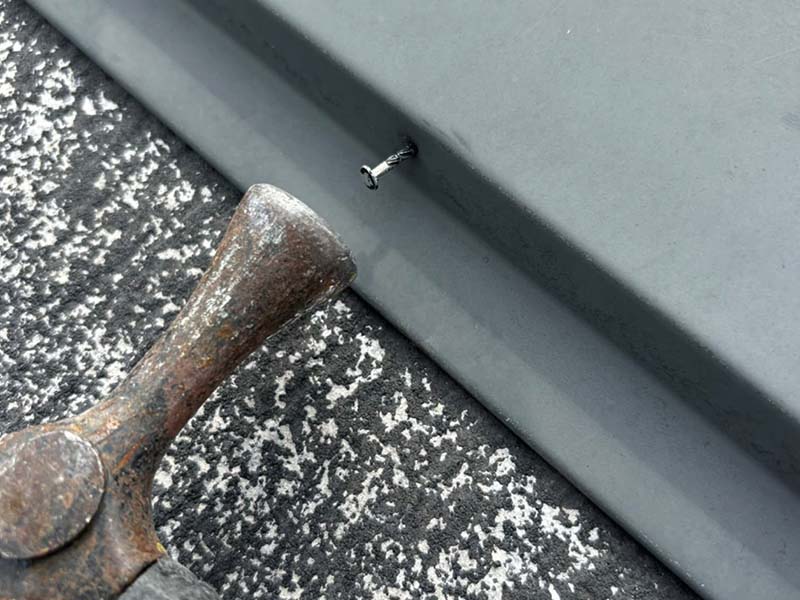 屋根の板金を止めるネジを金槌で打ち込む